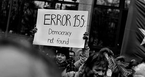 Frau hält ein Schild mit der Aufschrift "Error 155: Democracy not found" in die Luft.