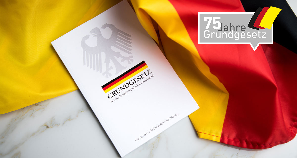 Grundgesetz-Buch der Bundesrepublik Deutschland auf Flagge.  Foto: Adobe Stock | Christin Klose. Logo 75 Jahre Grundgesetz. Grafik: LpB