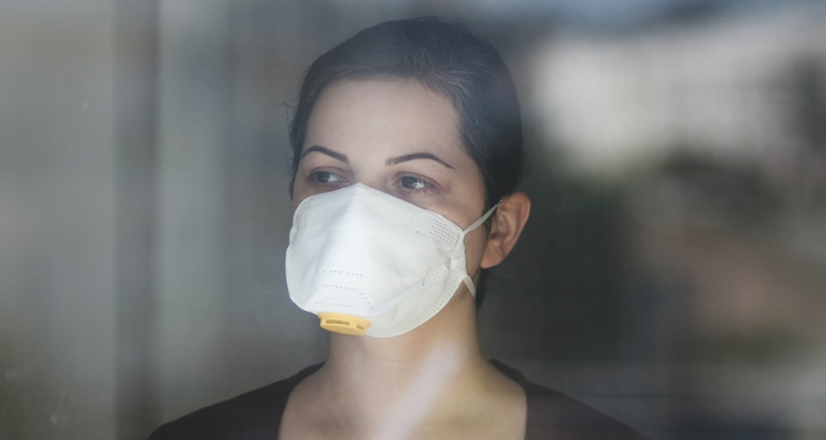 Frau mit Corona-Schutzmaske hinter einer Fensterscheibe. Foto: unsplash.com | Önder Örtel