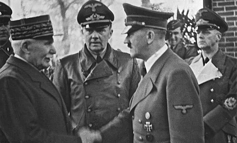 Philippe Pétain schüttelt Adolf Hitler die Hand. Zwischen beiden steht Dolmetscher Paul Schmidt, rechts Reichsaußenminister Joachim von Ribbentrop.